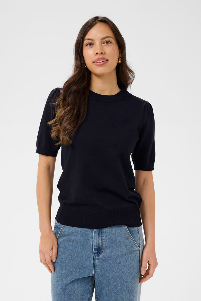 Woman wearing a navy blue sweater and blue jeans against a white background
