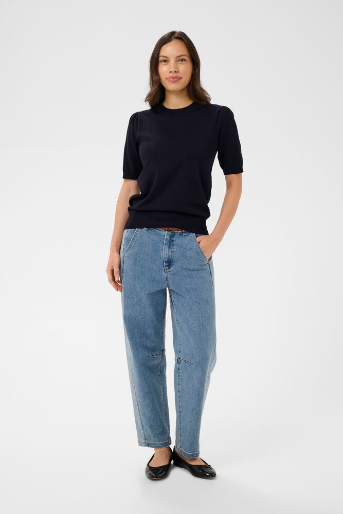 Woman wearing a navy blue top and blue jeans on a white background