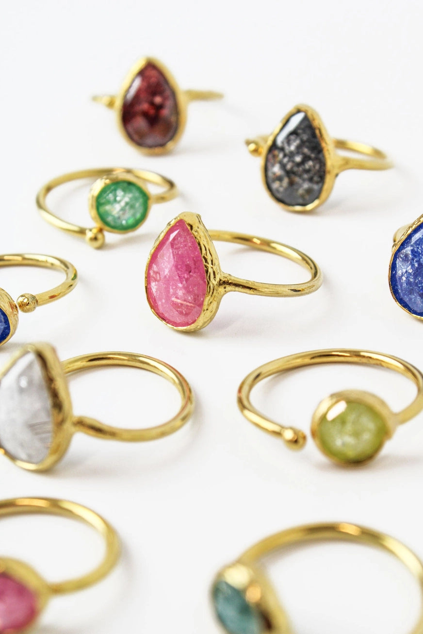 Collection of colorful gemstone rings with gold bands on a white background
