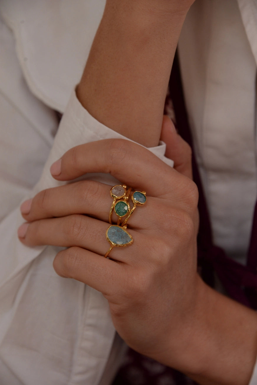 Close-up of a hand wearing multiple gold rings with green gemstones on a neutral background