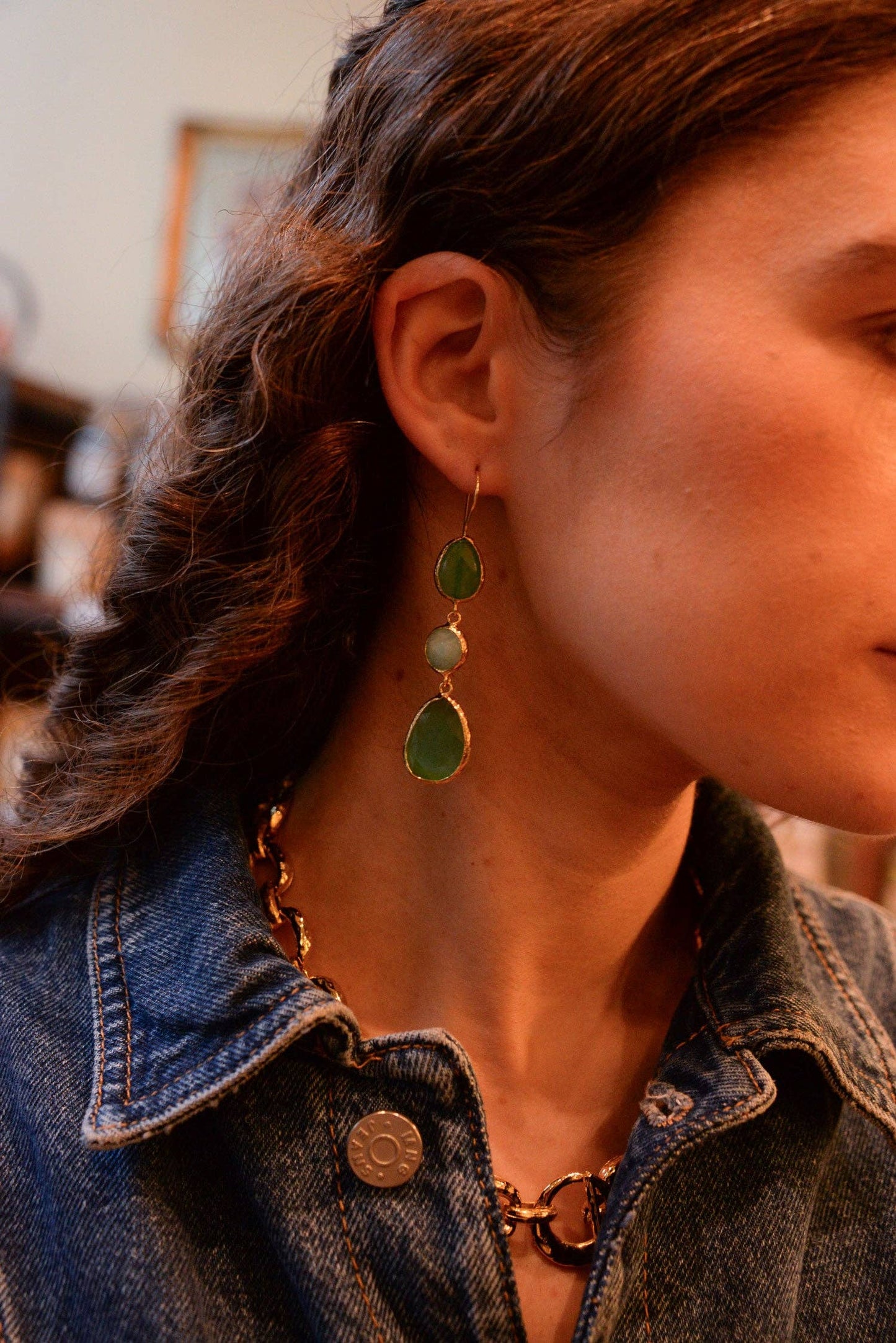 Close-up of a person wearing green earrings with a denim jacket.