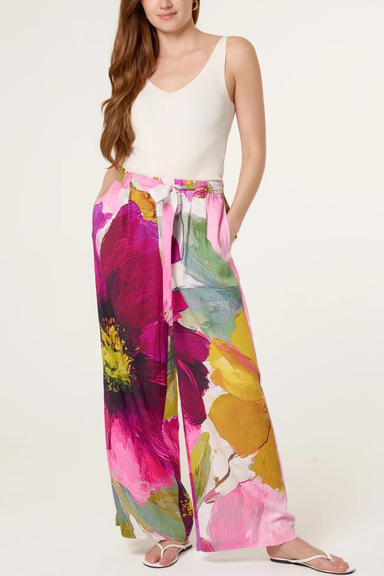 Woman wearing a white sleeveless top and colorful floral pants on a white background