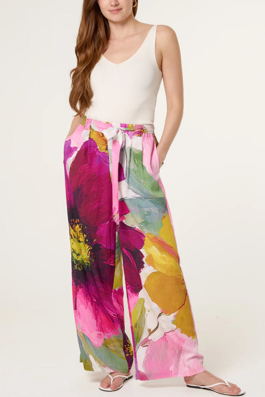 Woman wearing a white sleeveless top and colorful floral pants on a white background