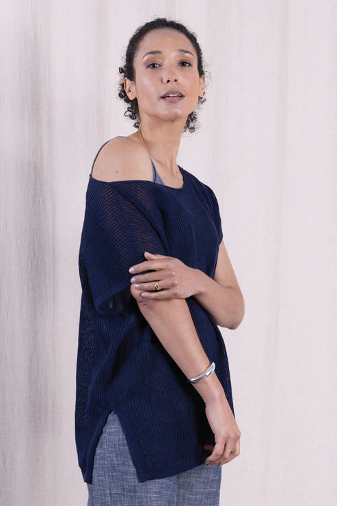 Woman wearing a navy blue off-shoulder top against a light curtain background