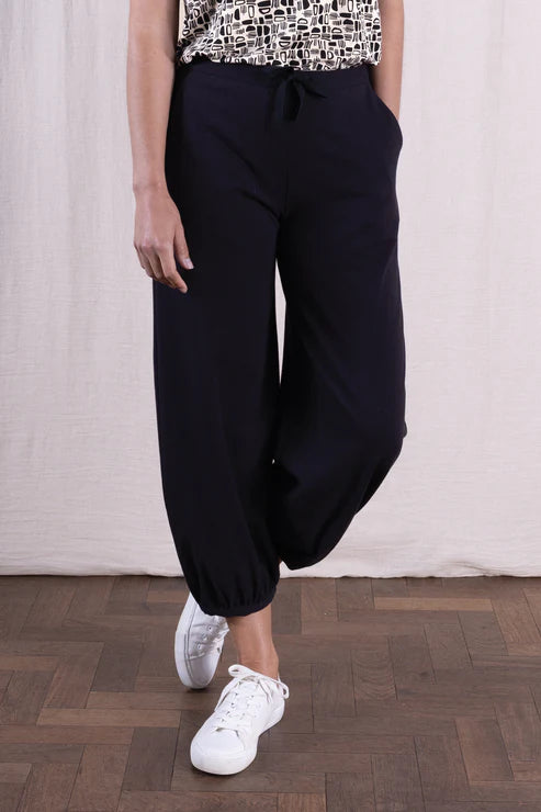 Person wearing black wide-leg pants and white sneakers on a wooden floor.