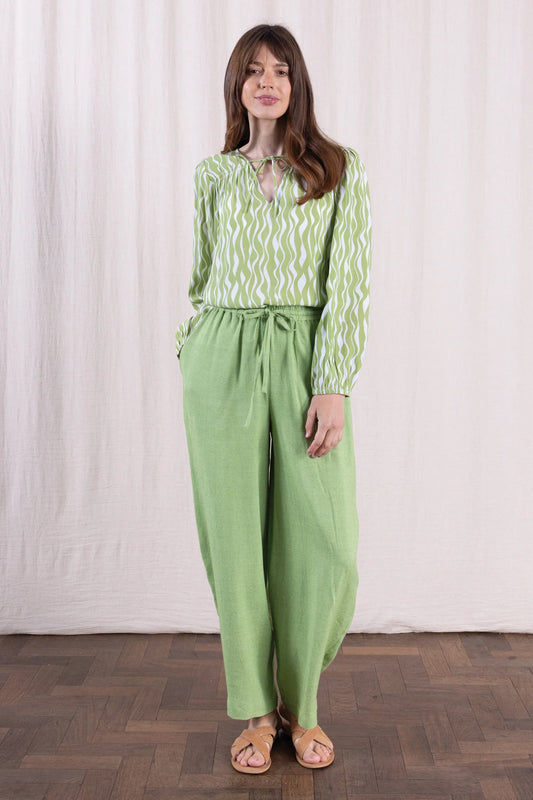Woman wearing a green patterned top and matching pants against a white background