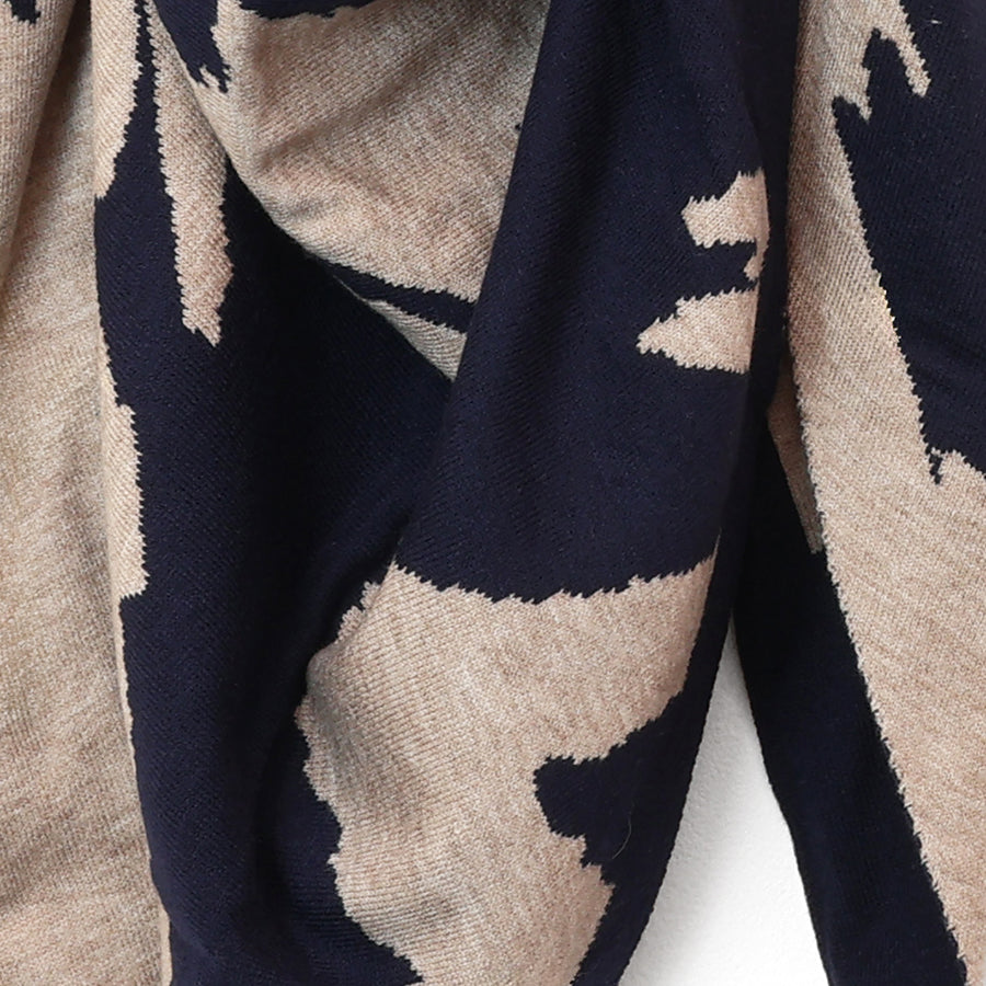 A close-up of a knit fabric scarf or shawl with a bold abstract pattern in dark navy blue and warm beige.