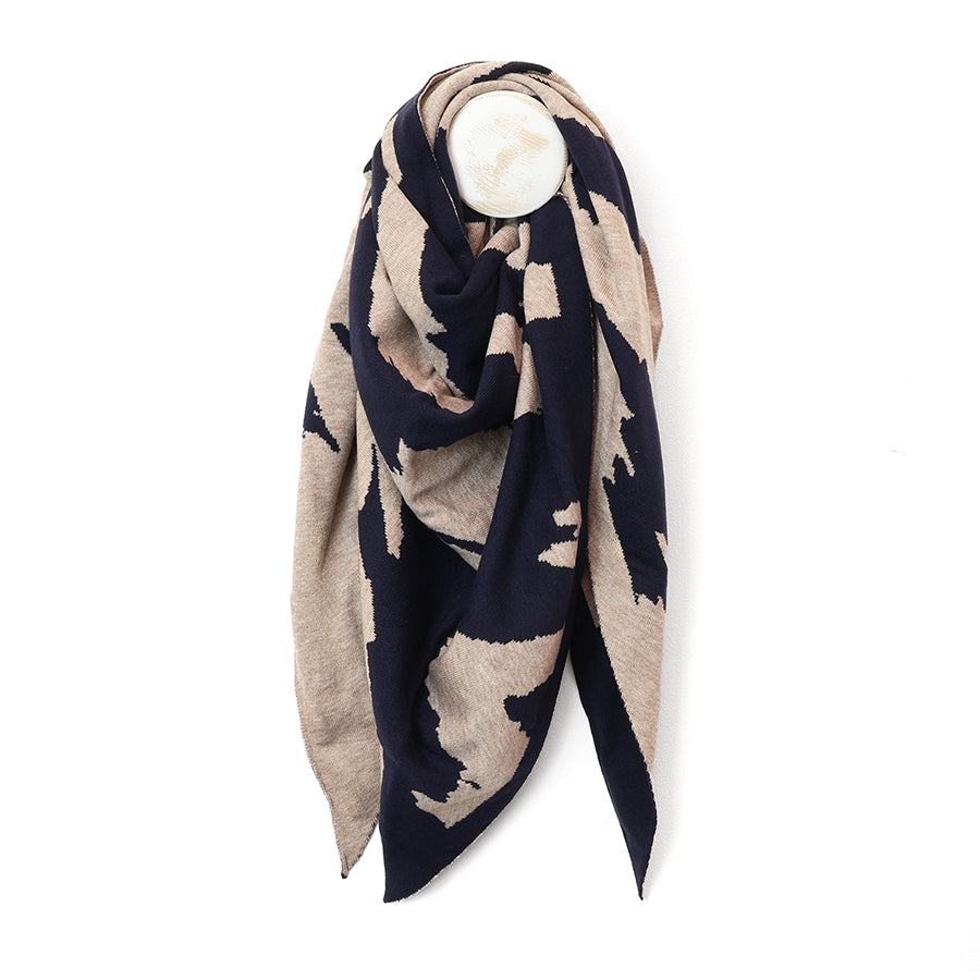 A square knit scarf draped on a white mannequin torso, featuring an abstract ikat-style pattern in dark navy blue and warm beige.