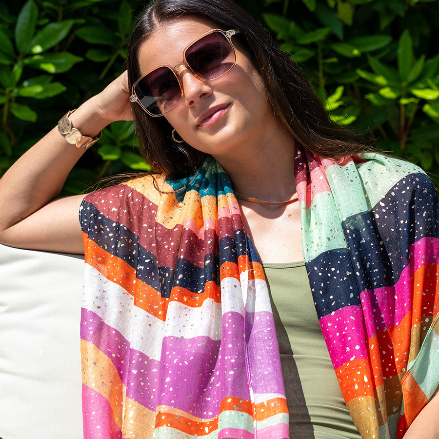 Woman wearing a colorful striped scarf with sunglasses and a watch, sitting outdoors.