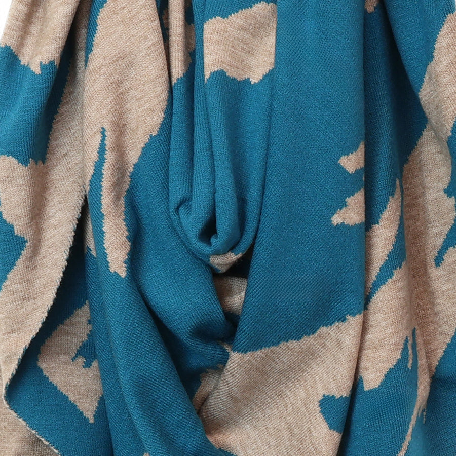 A close-up of a knitted fabric with an abstract ikat pattern in teal blue and warm beige.
