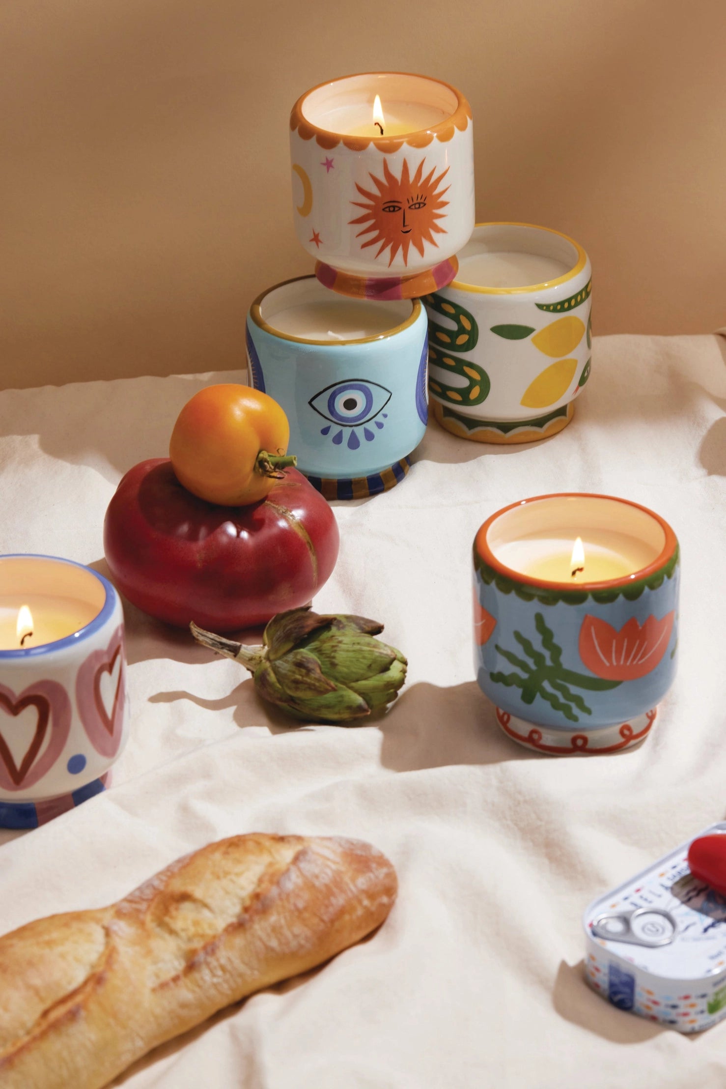 Colorful candles with decorative designs on a white cloth with bread and fruit.