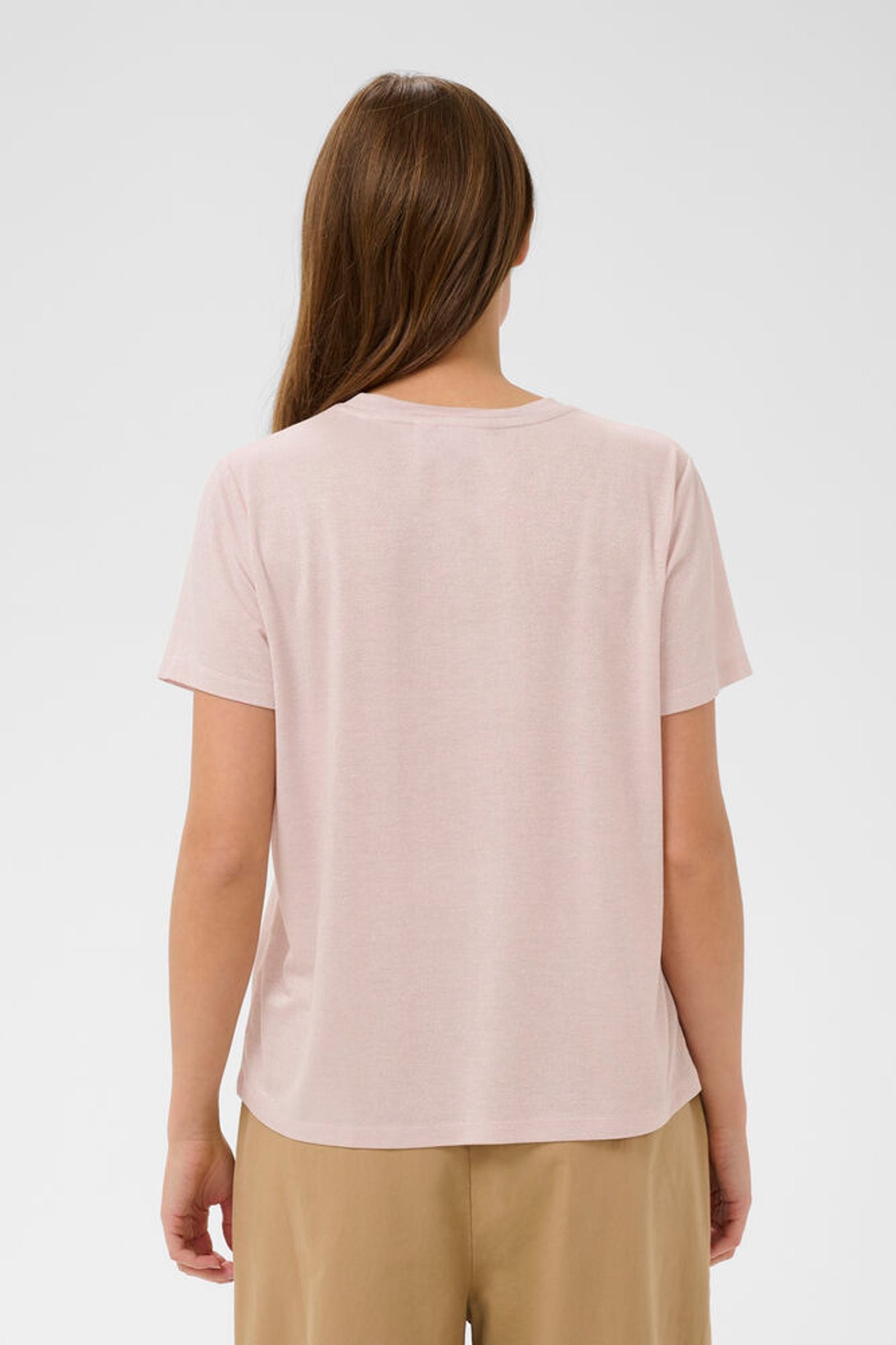 Woman wearing a light pink t-shirt and beige pants on a white background