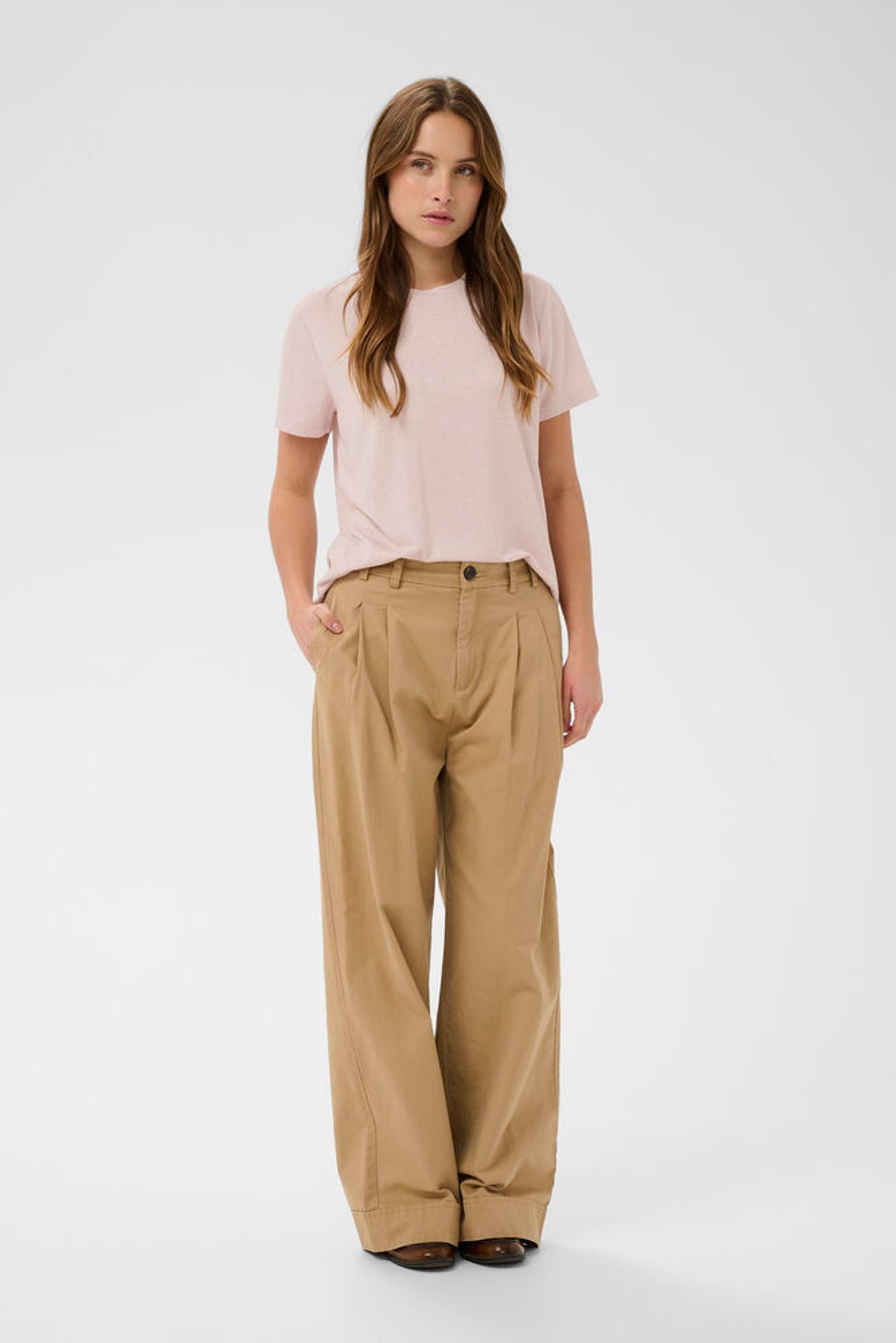 Woman wearing a light pink t-shirt and beige pants on a white background