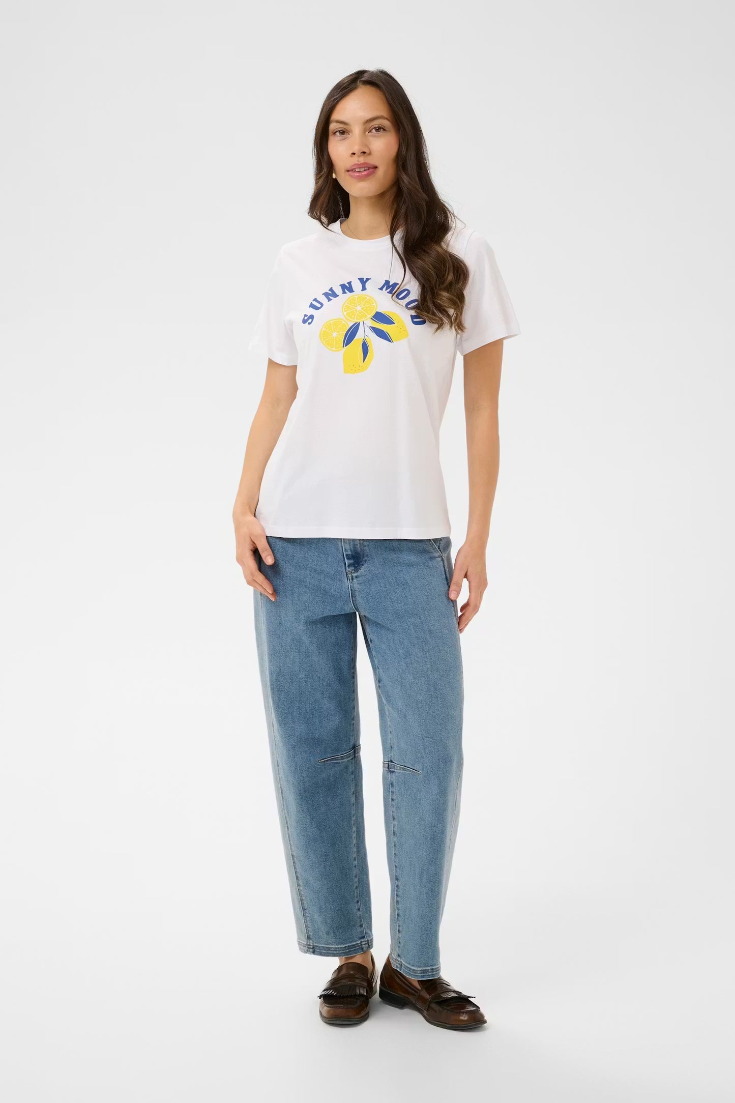 Woman wearing a white t-shirt with a colorful graphic and blue jeans on a white background