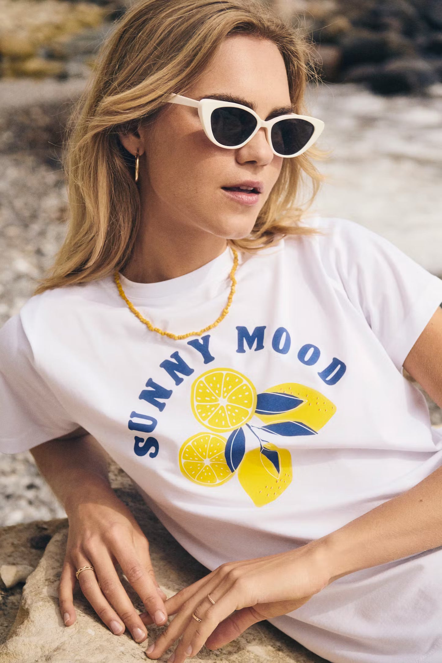 Woman wearing a 'Sunny Mood' t-shirt with lemons on a rocky surface