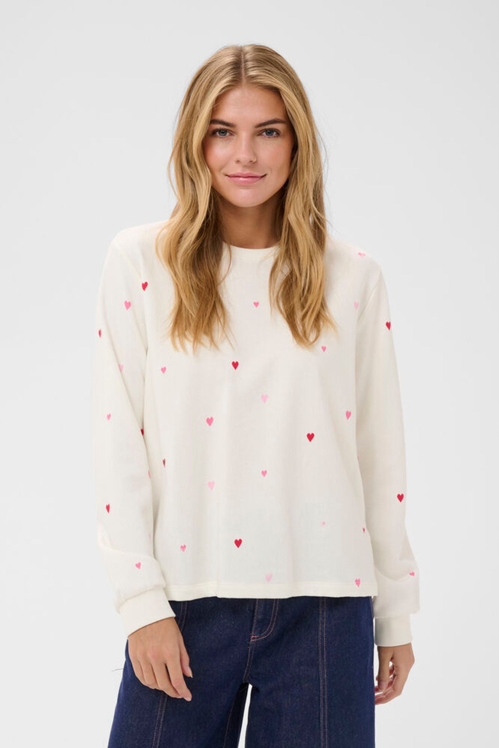 Woman wearing a cream sweater with red heart patterns on a white background