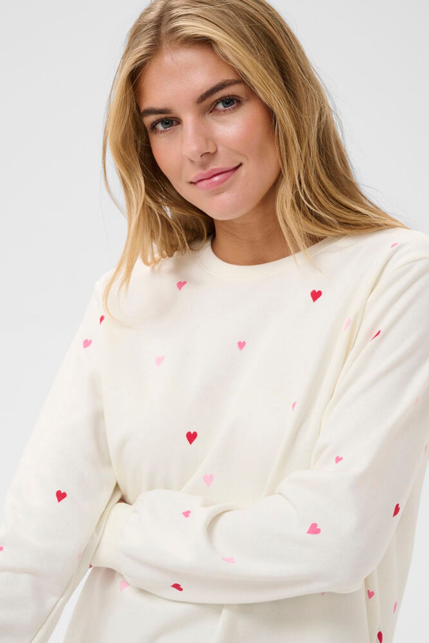 Woman wearing a cream-colored sweater with red heart patterns on a white background