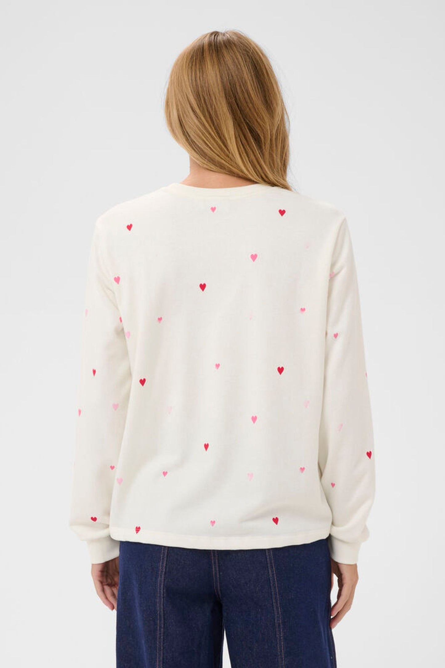 Person wearing a white sweater with red heart patterns on a plain background