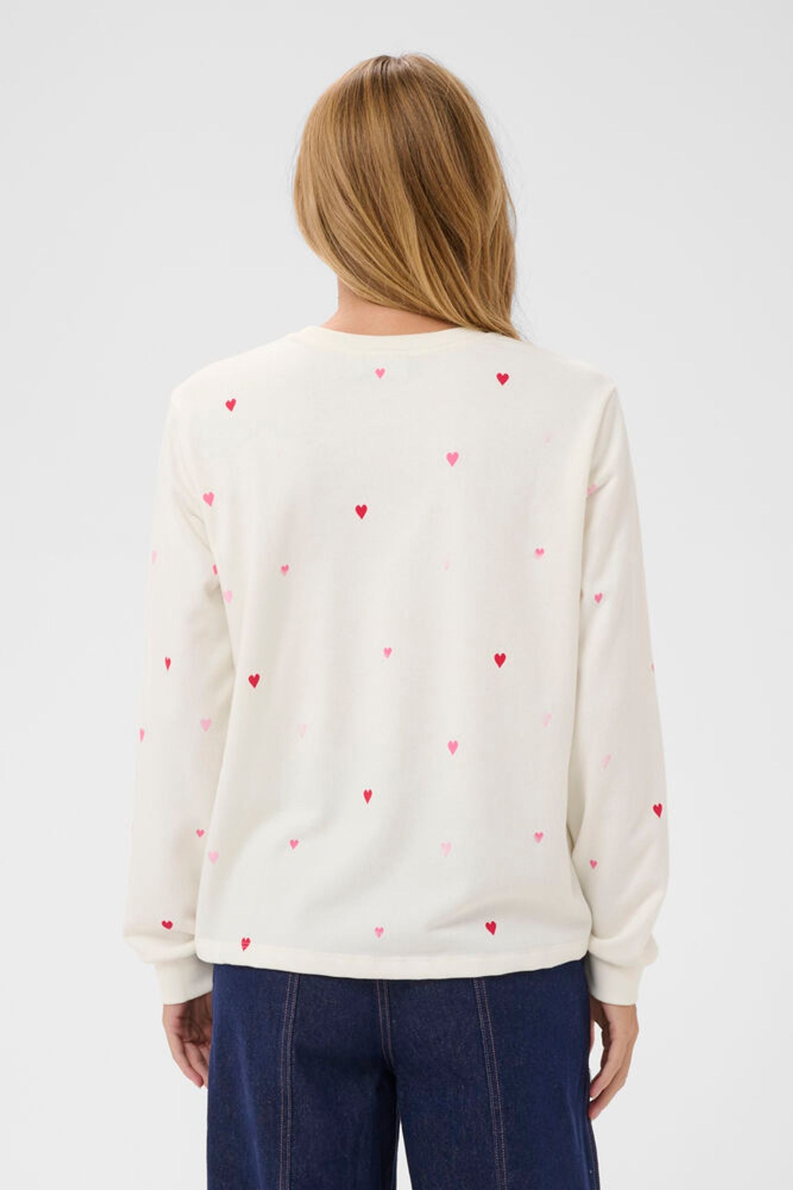 Person wearing a white sweater with red heart patterns on a plain background