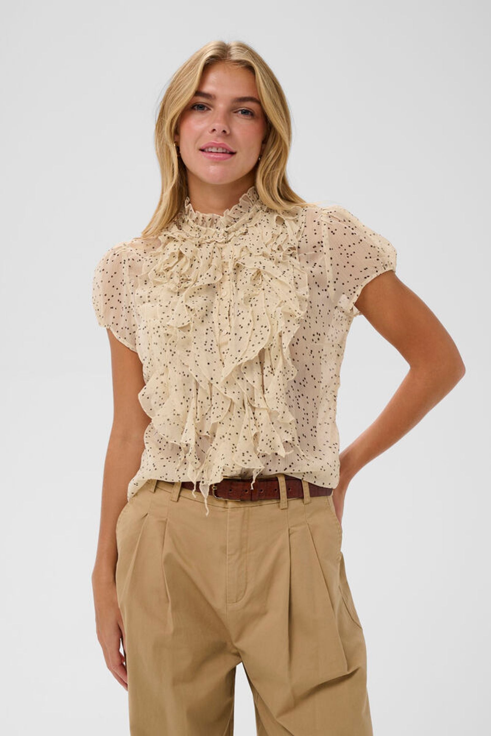 Woman wearing a beige floral blouse and beige pants on a white background