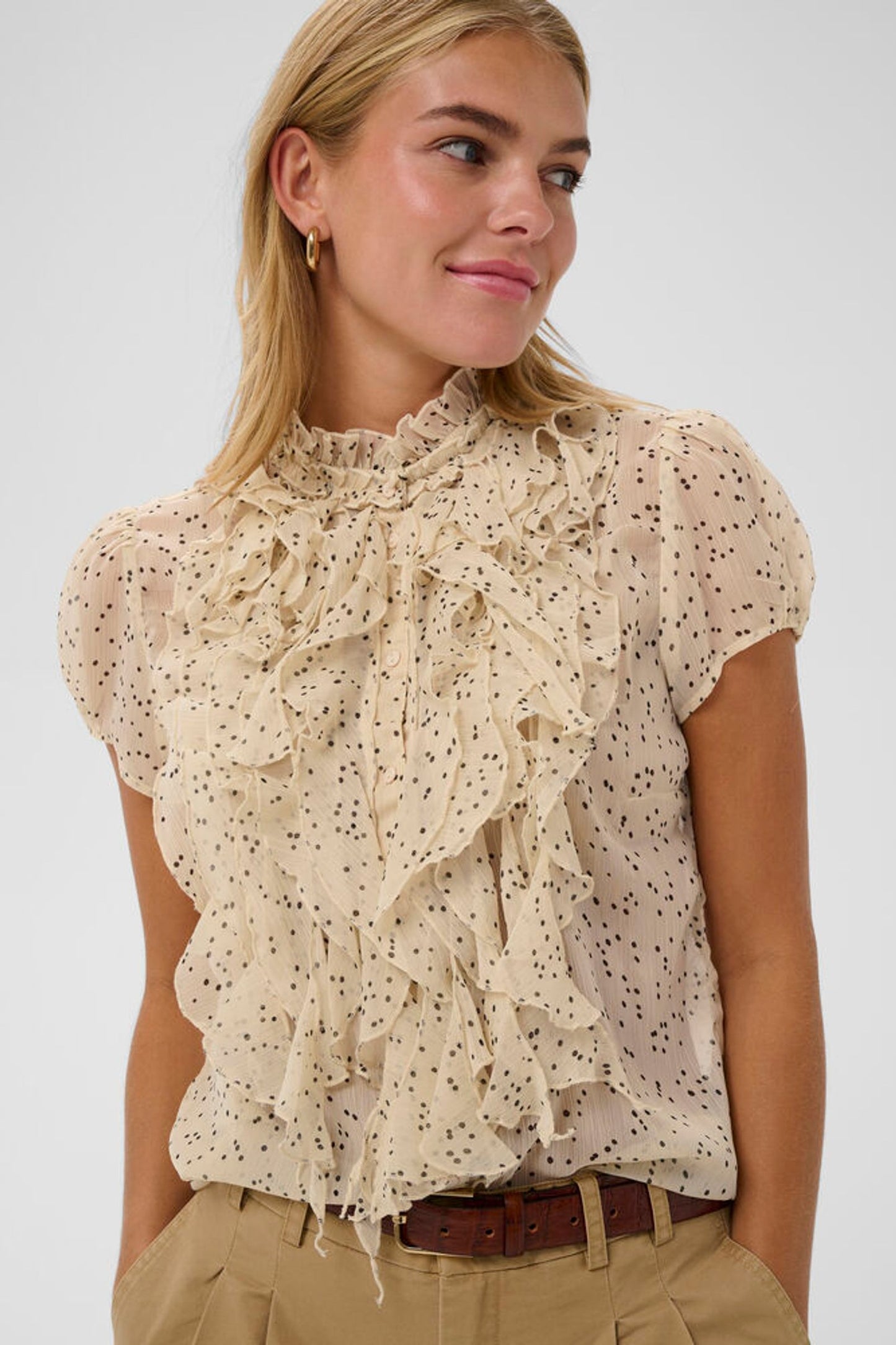 Woman wearing a beige ruffled blouse with a white background