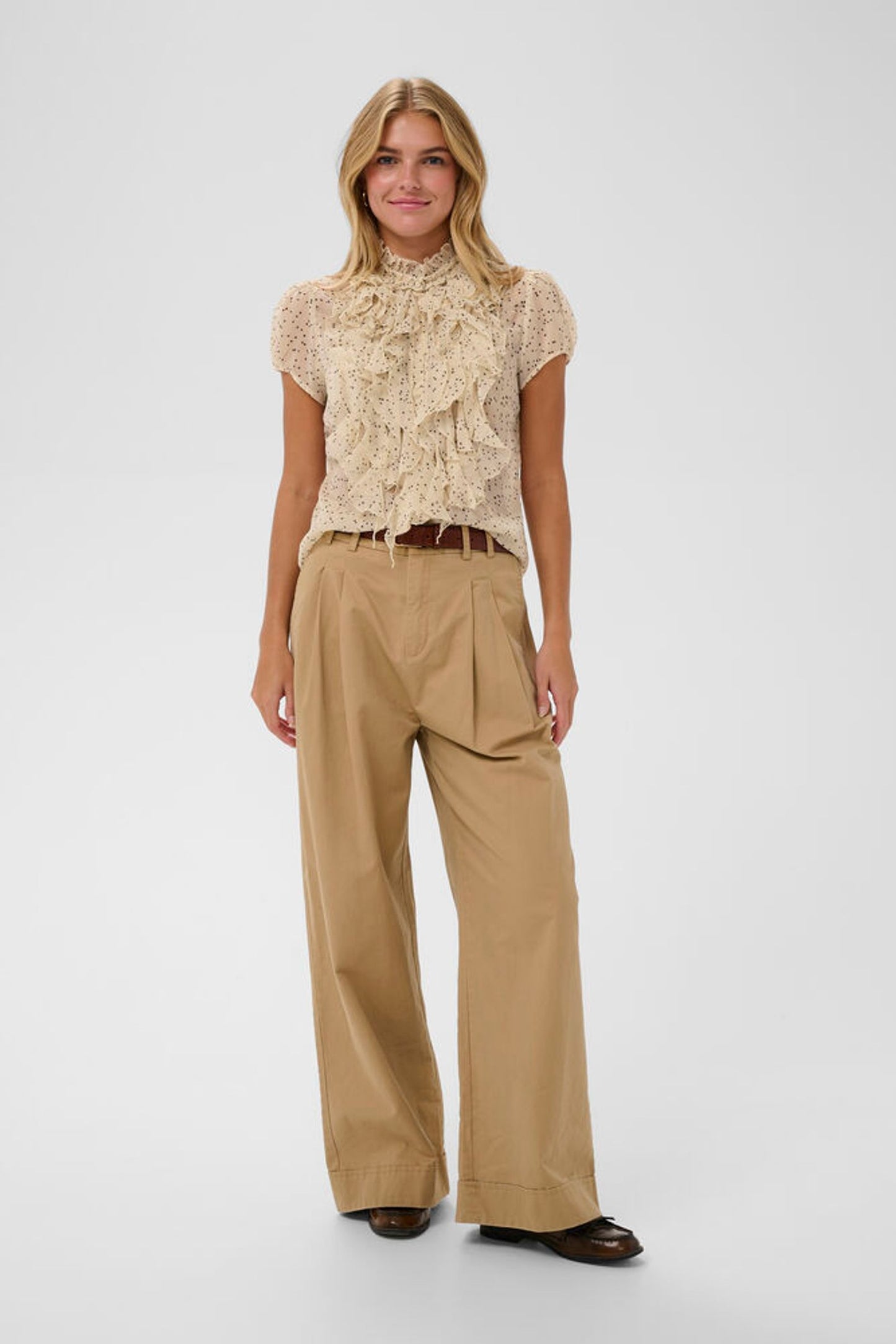 Woman wearing a beige lace top and tan pants on a white background