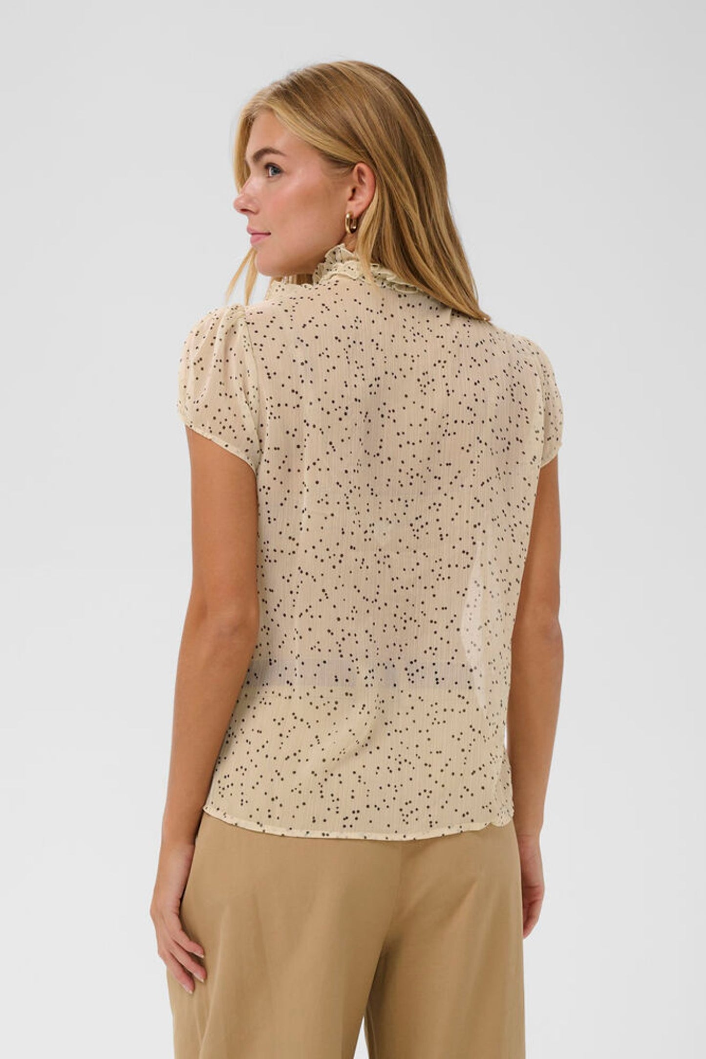 Woman wearing a beige patterned blouse and beige pants on a white background