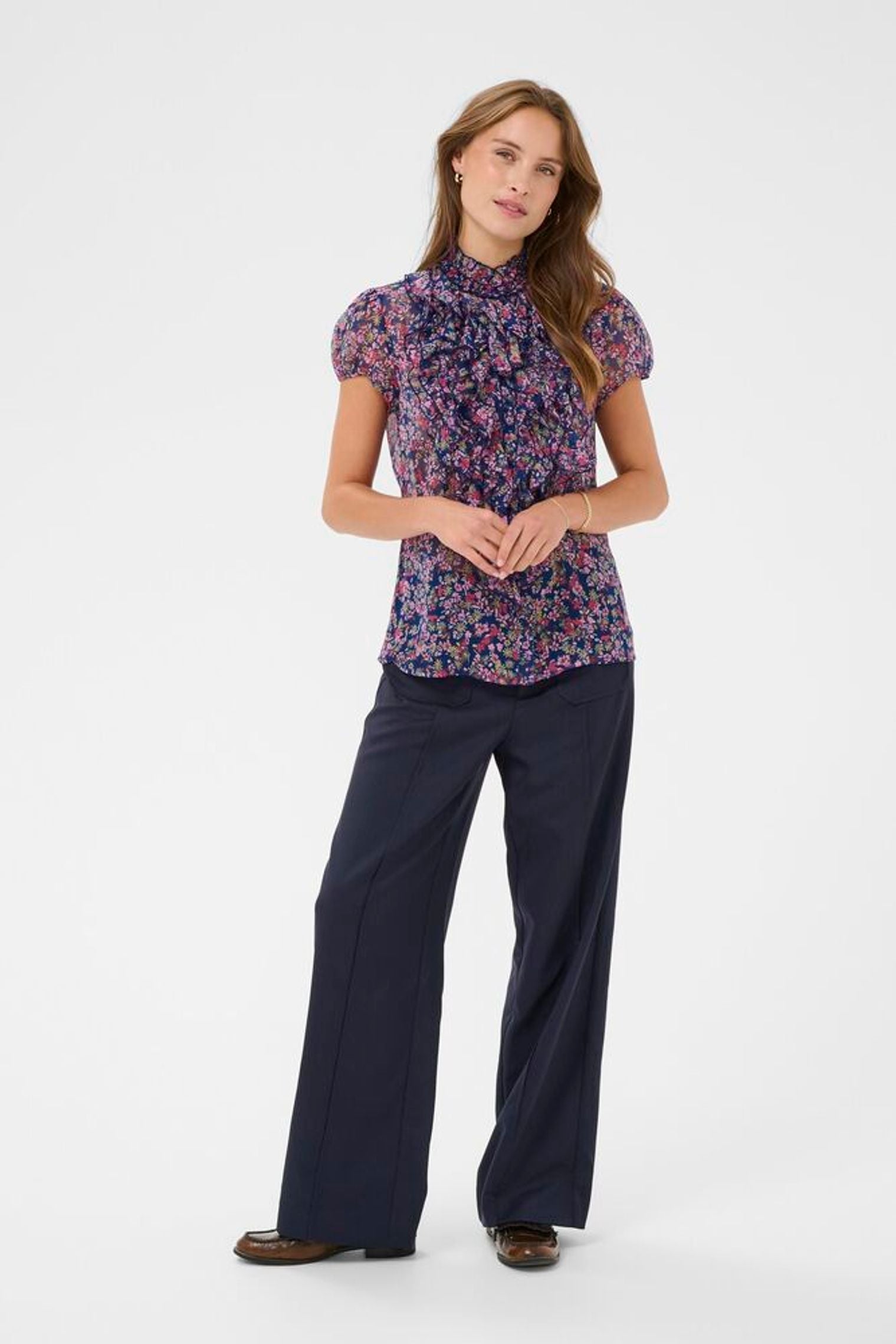 Woman wearing a floral blouse and navy pants on a white background