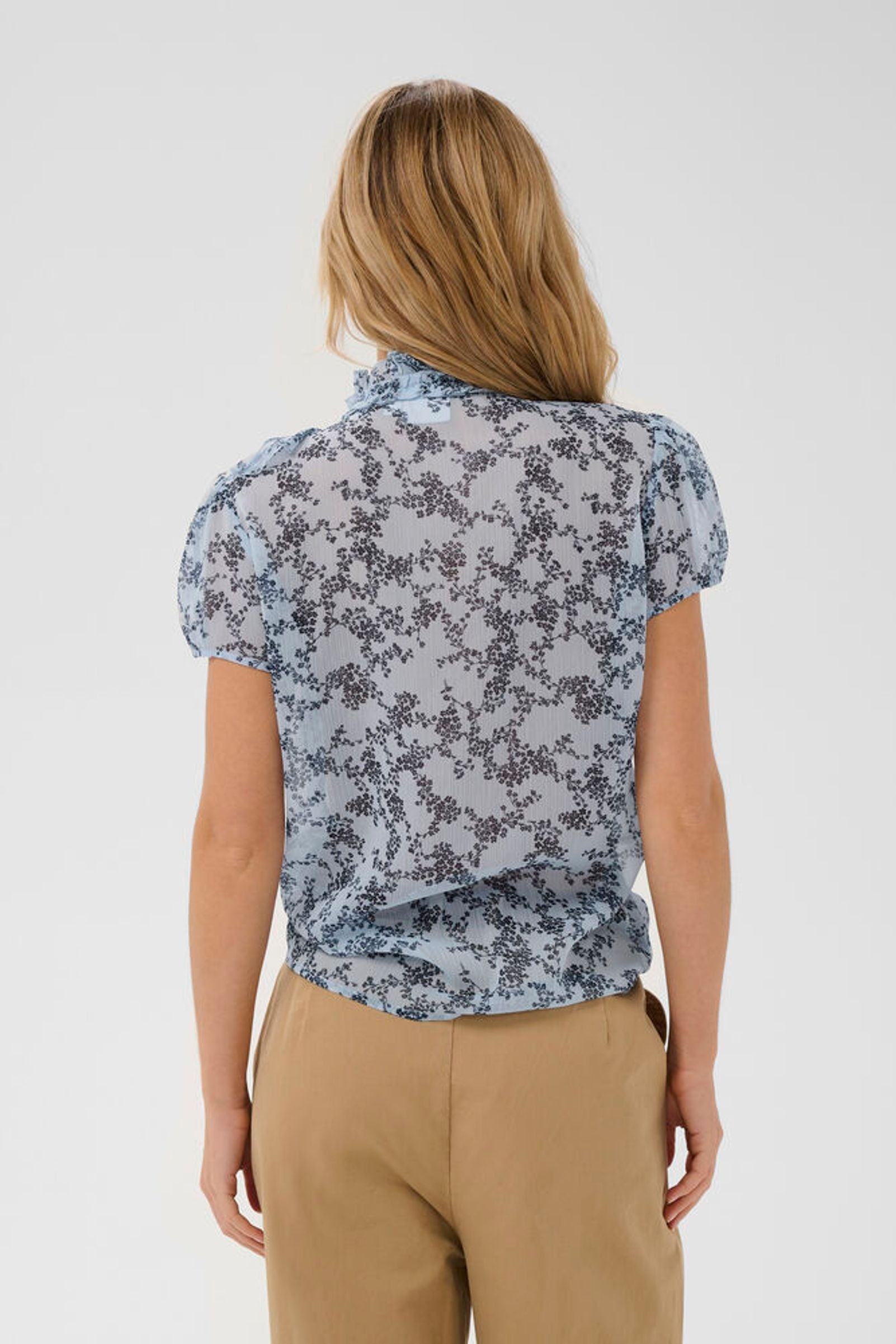 Woman wearing a floral blouse and beige pants on a white background