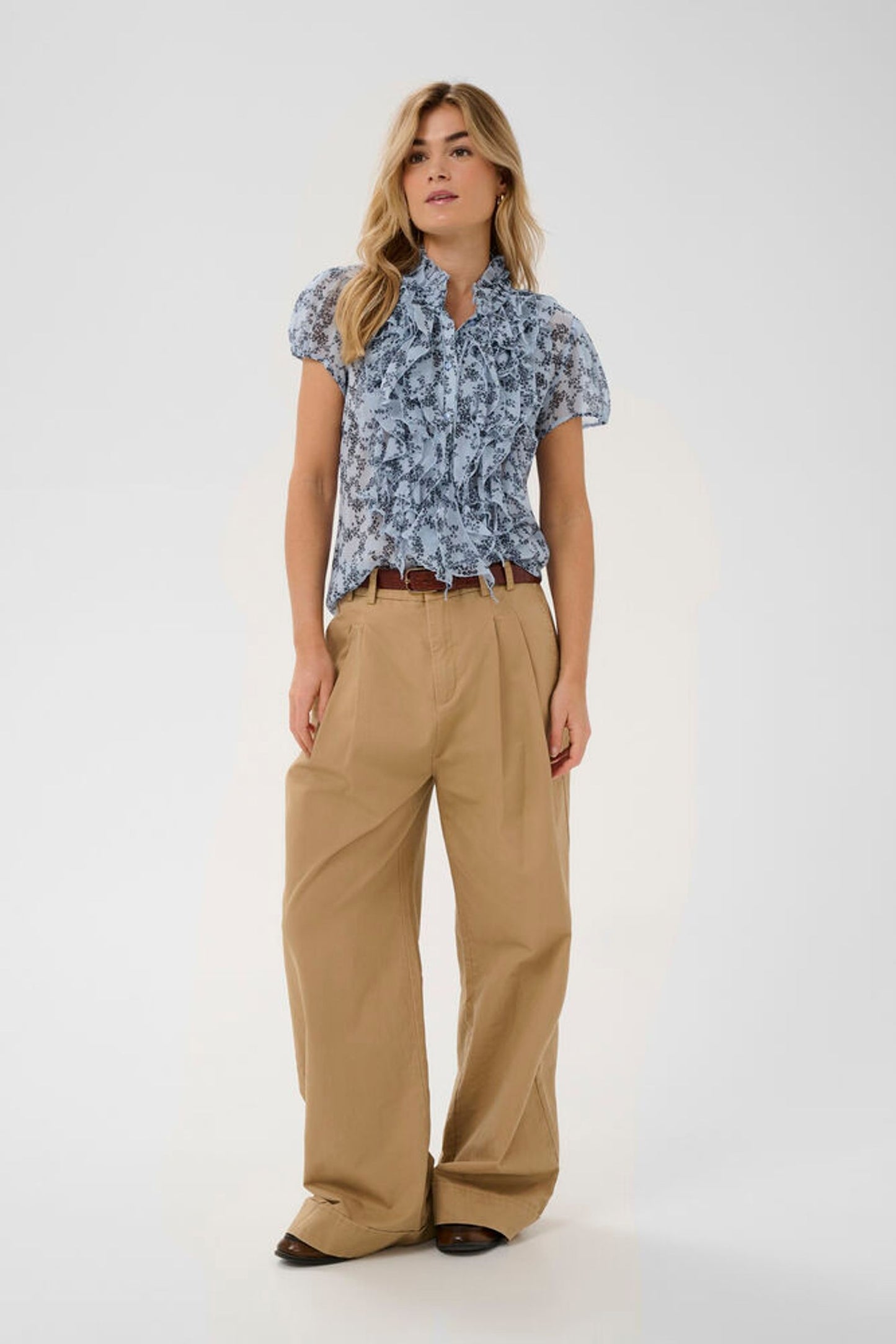 Woman wearing a blue floral blouse and beige pants on a white background