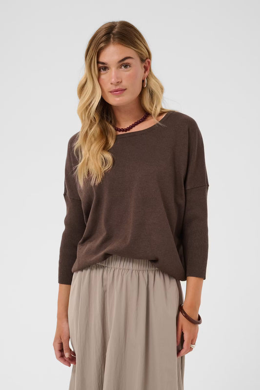 A woman modeling a brown long-sleeve knit top with a wide boat neckline, paired with light beige wide-leg pants, against a plain light gray studio background.