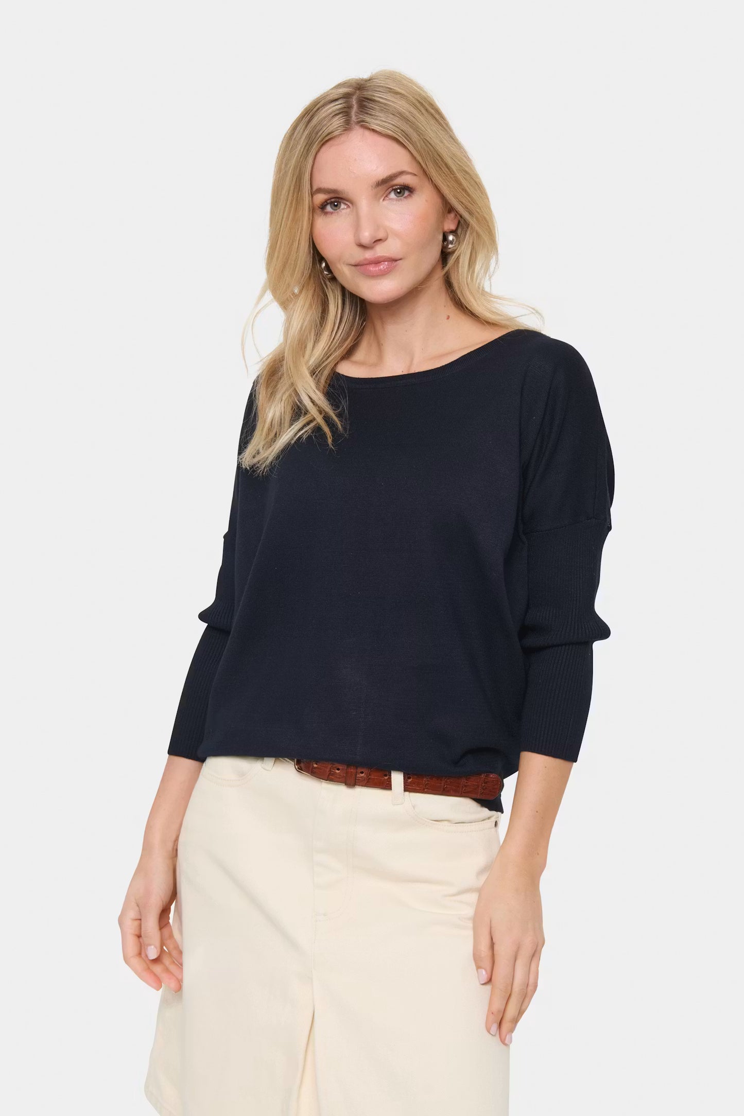 Woman wearing a navy top and beige pants on a white background
