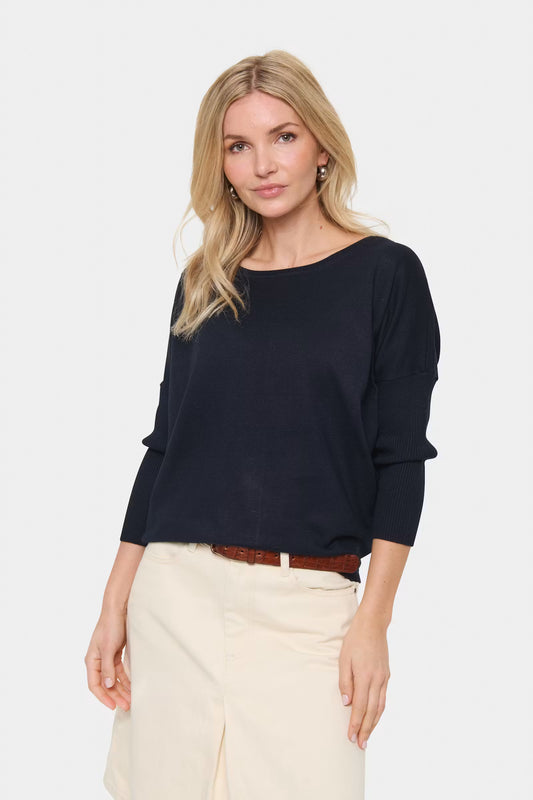 Woman wearing a navy top and beige pants on a white background