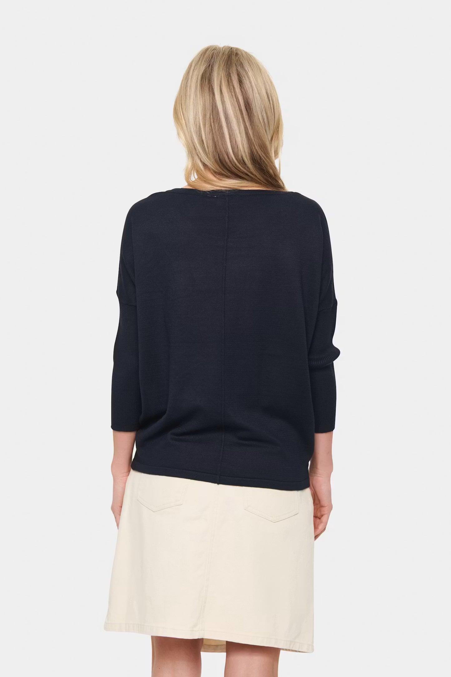 Woman wearing a navy blue sweater and beige skirt on a white background