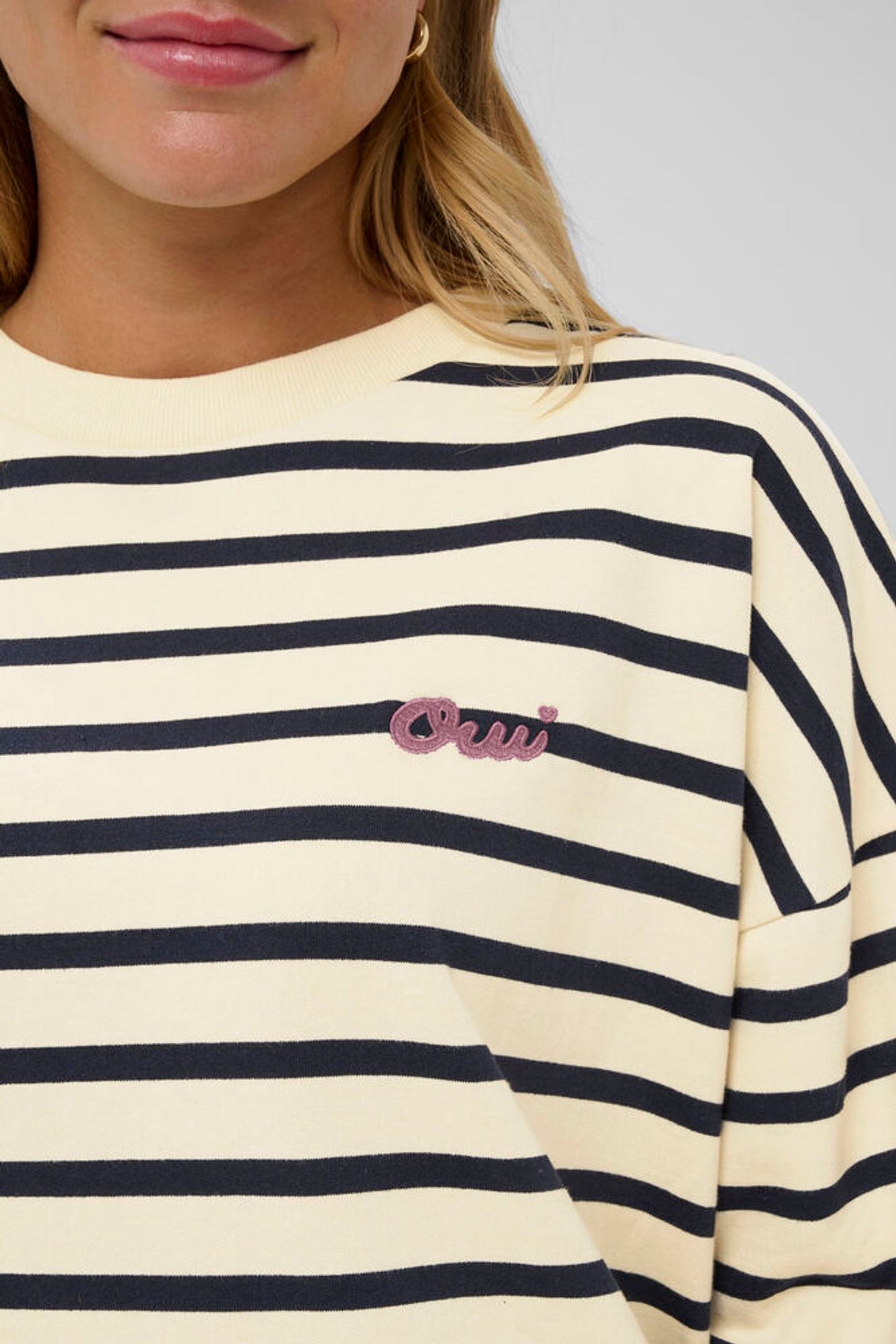 Close-up of a person wearing a cream and navy striped shirt with a pink logo.