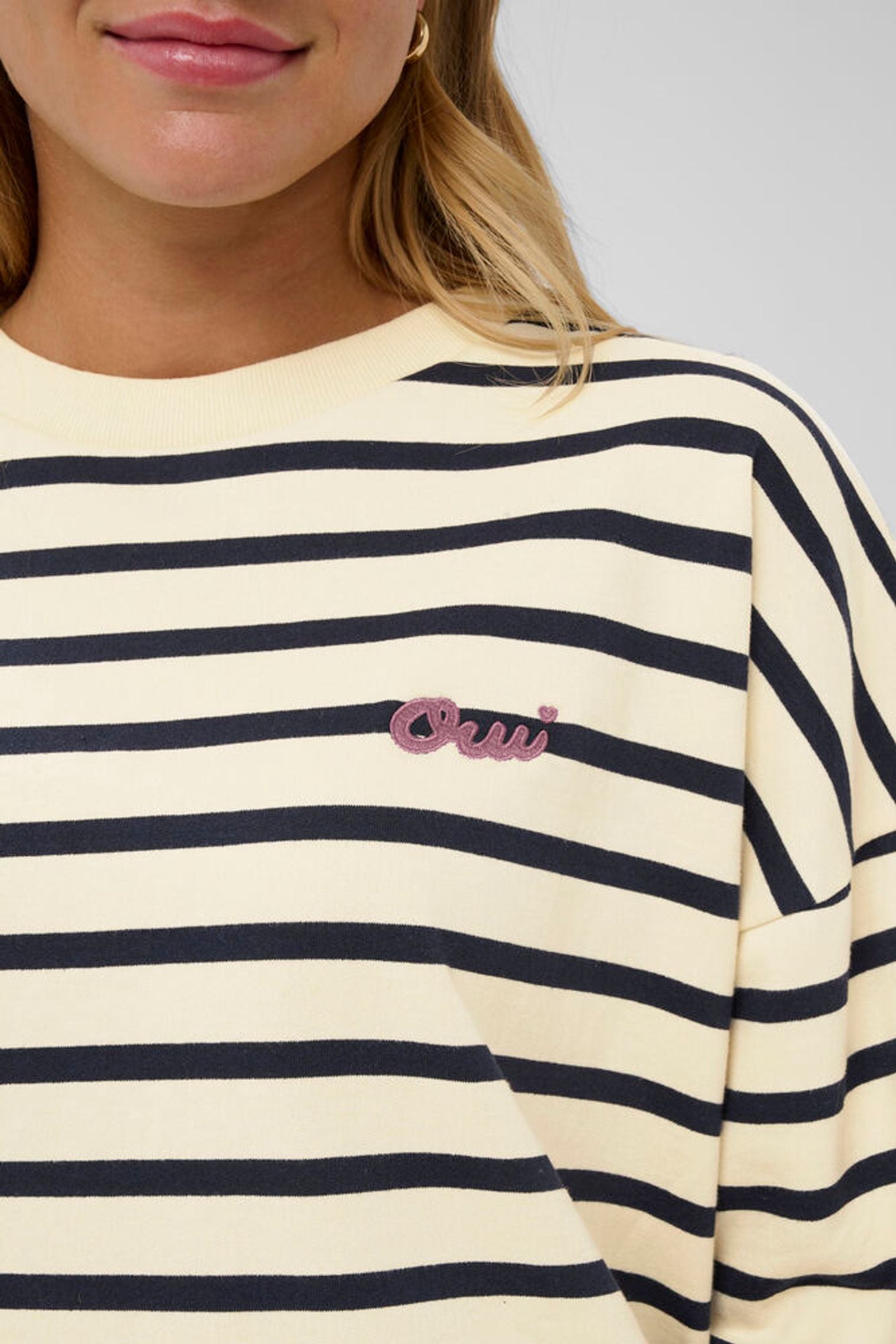 Close-up of a person wearing a cream and navy striped shirt with a pink logo.