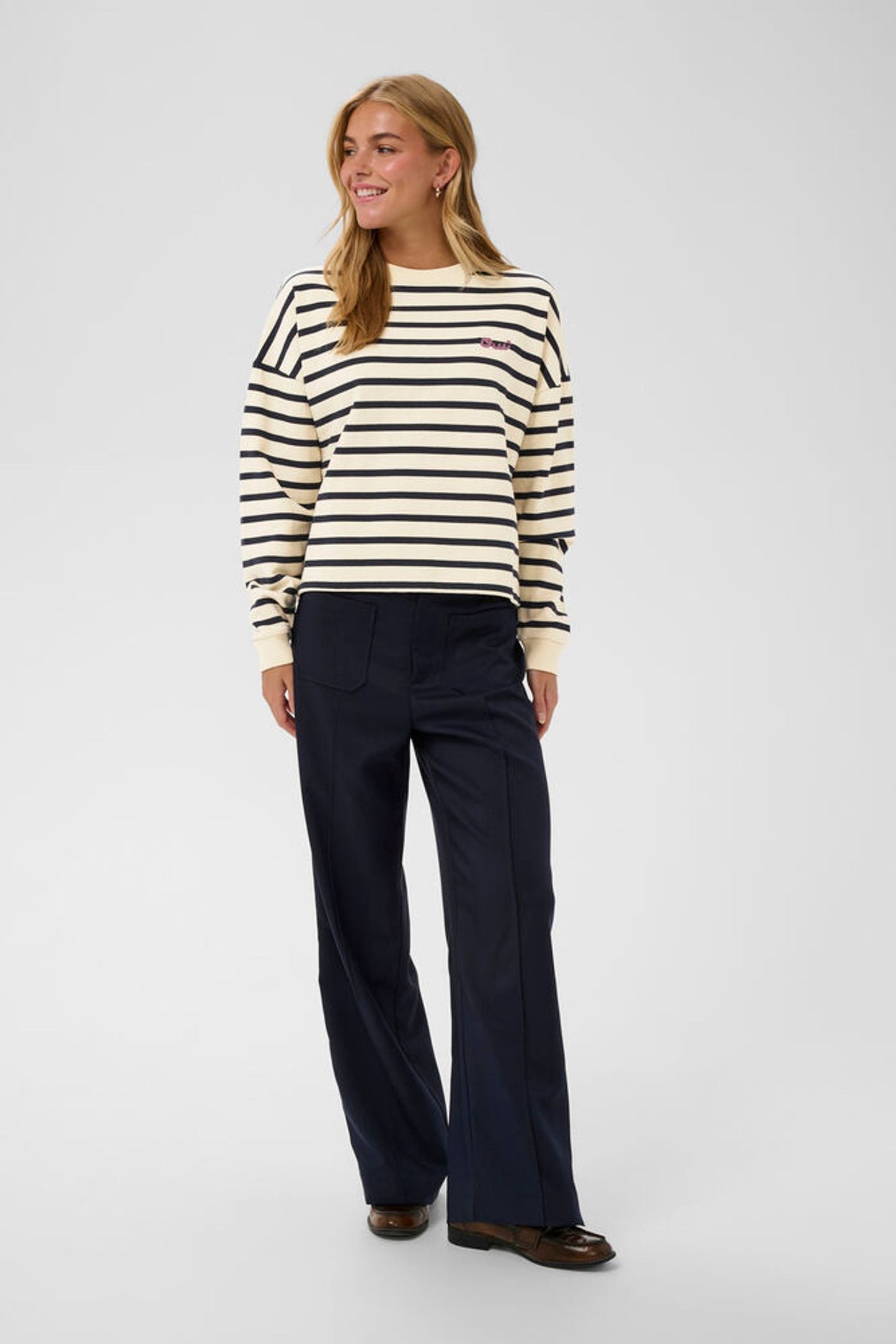 Model in striped sweatshirt with navy trousers