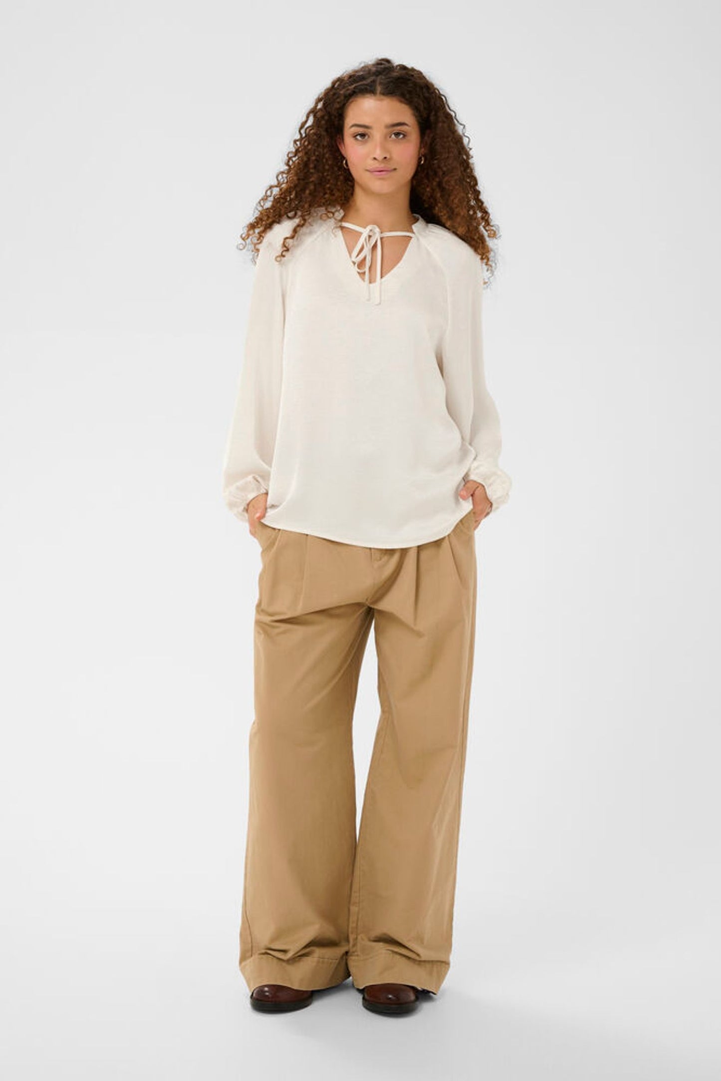 Woman wearing a white blouse and beige pants on a white background