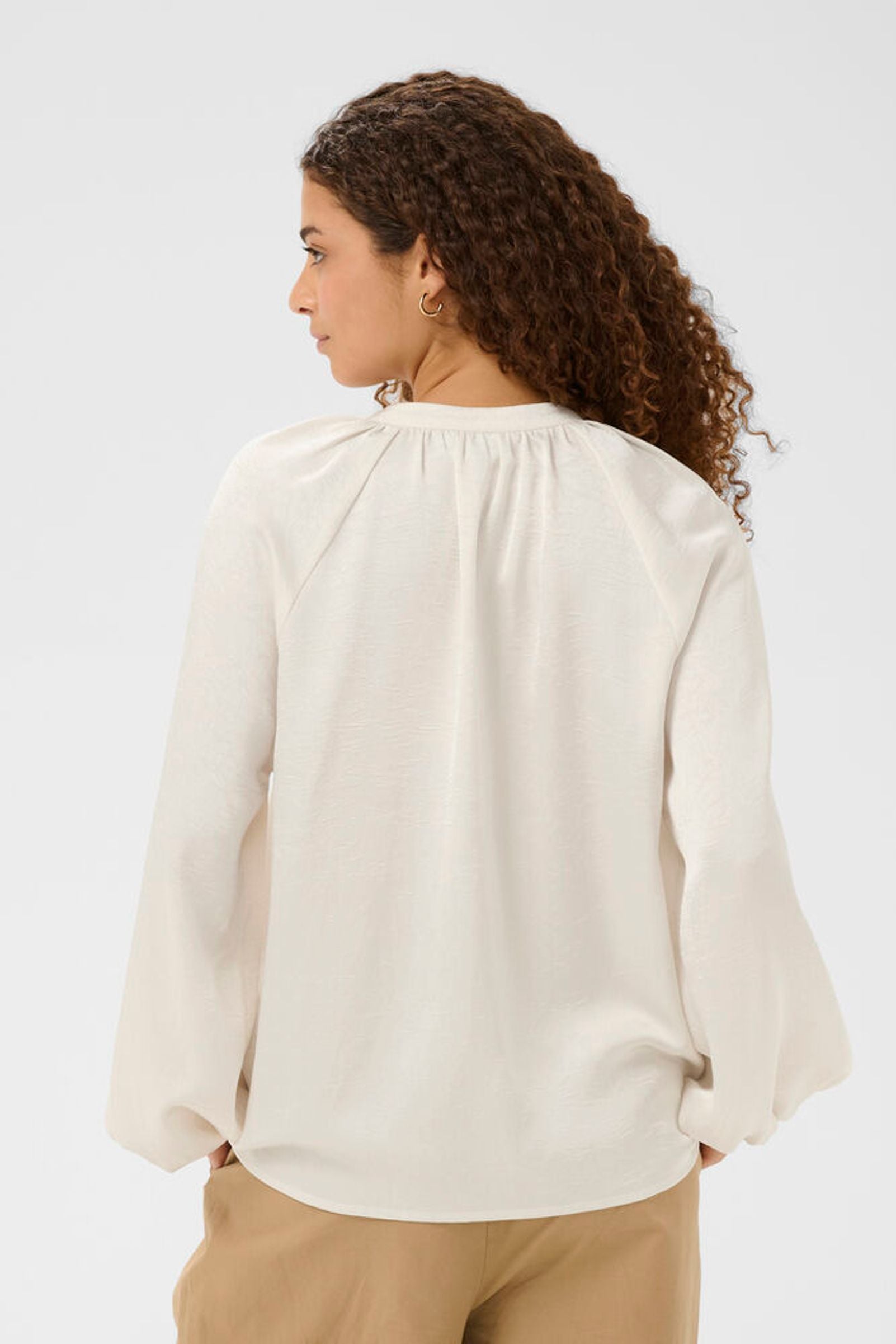 Woman wearing a beige blouse with long sleeves on a white background