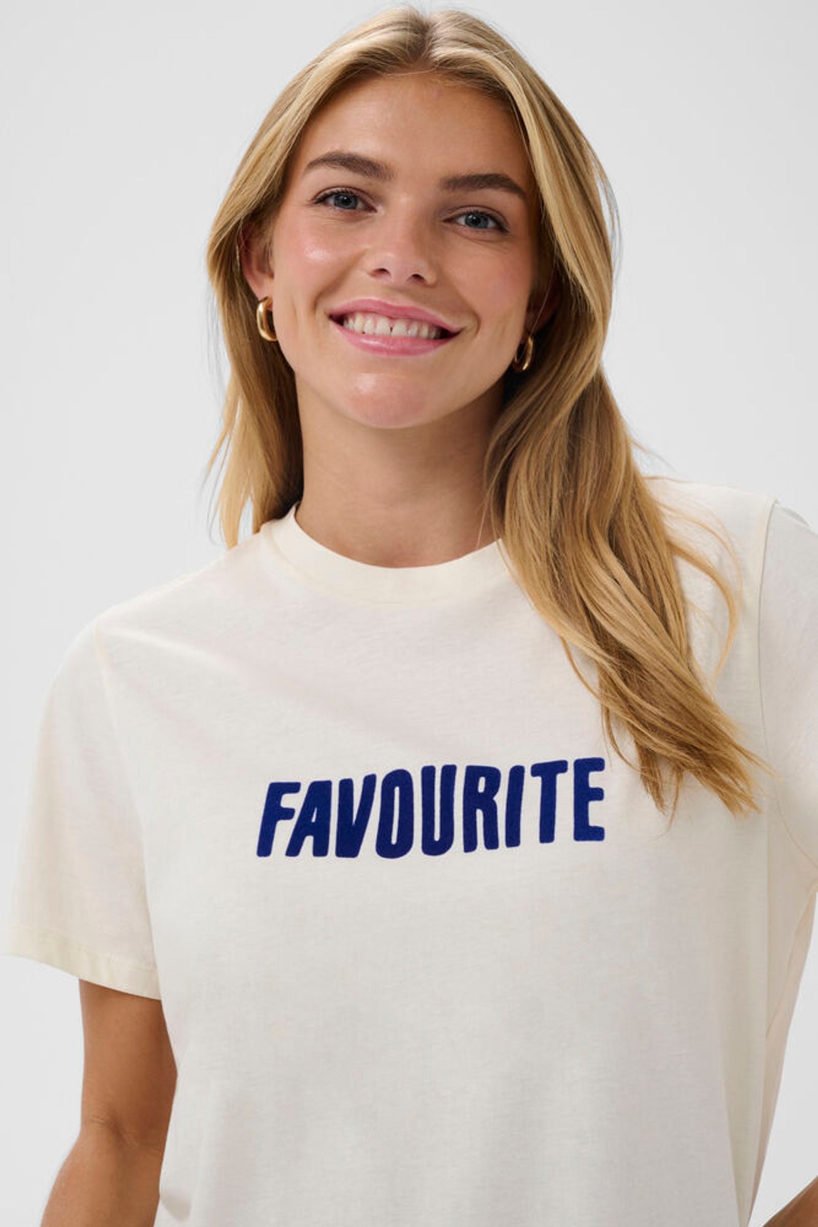 Woman wearing a white t-shirt with 'FAVOURITE' printed in blue on a plain background