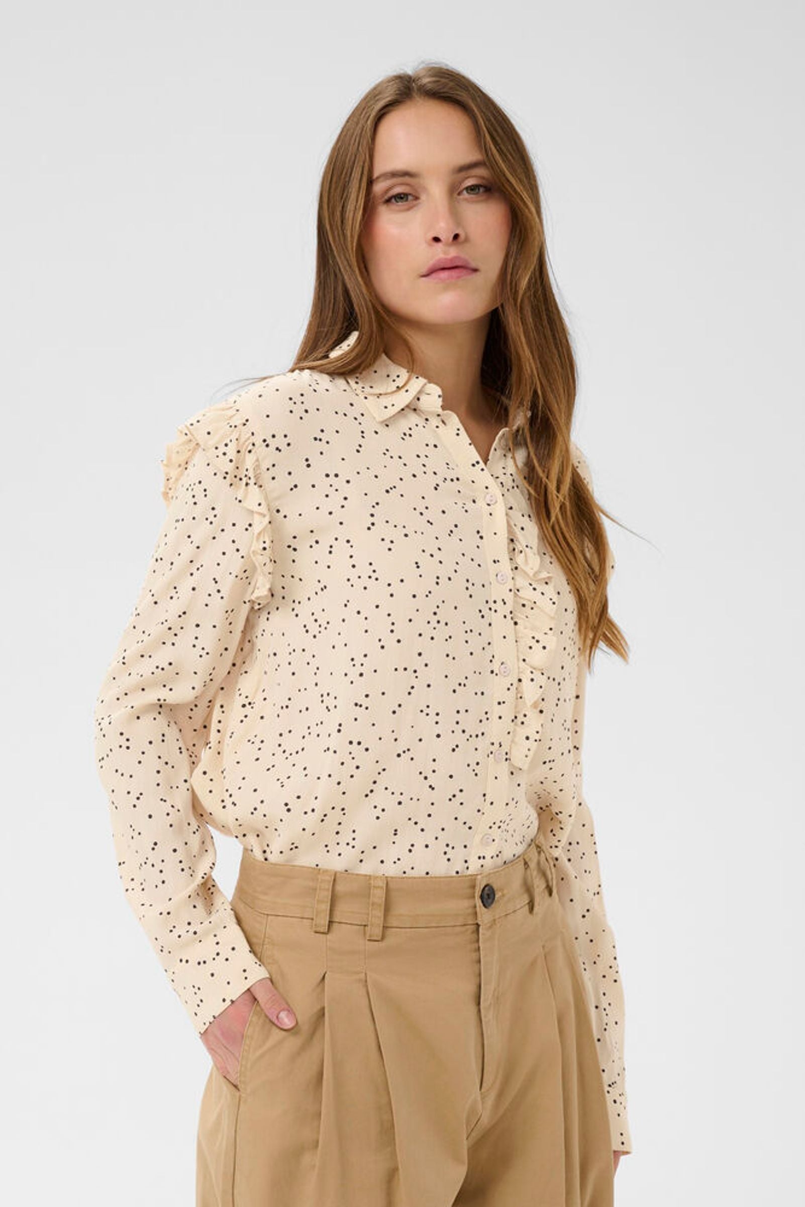 Woman wearing a beige floral blouse and beige pants against a white background