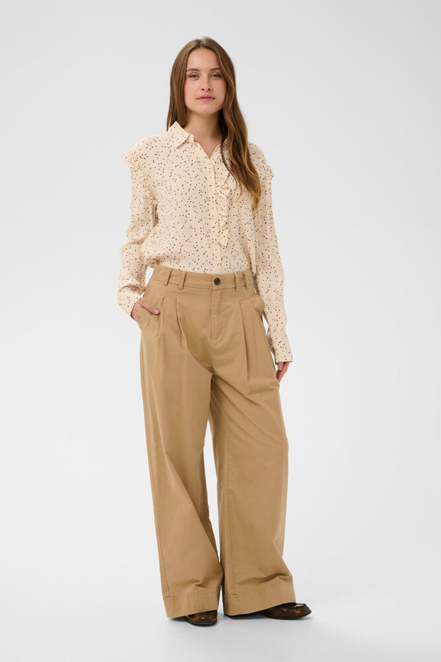 Woman wearing a beige blouse and tan pants on a white background