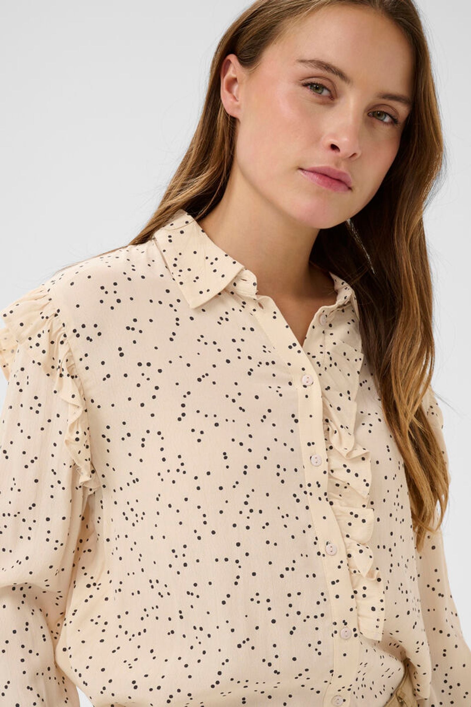 Woman wearing a beige blouse with a subtle polka dot pattern on a plain background