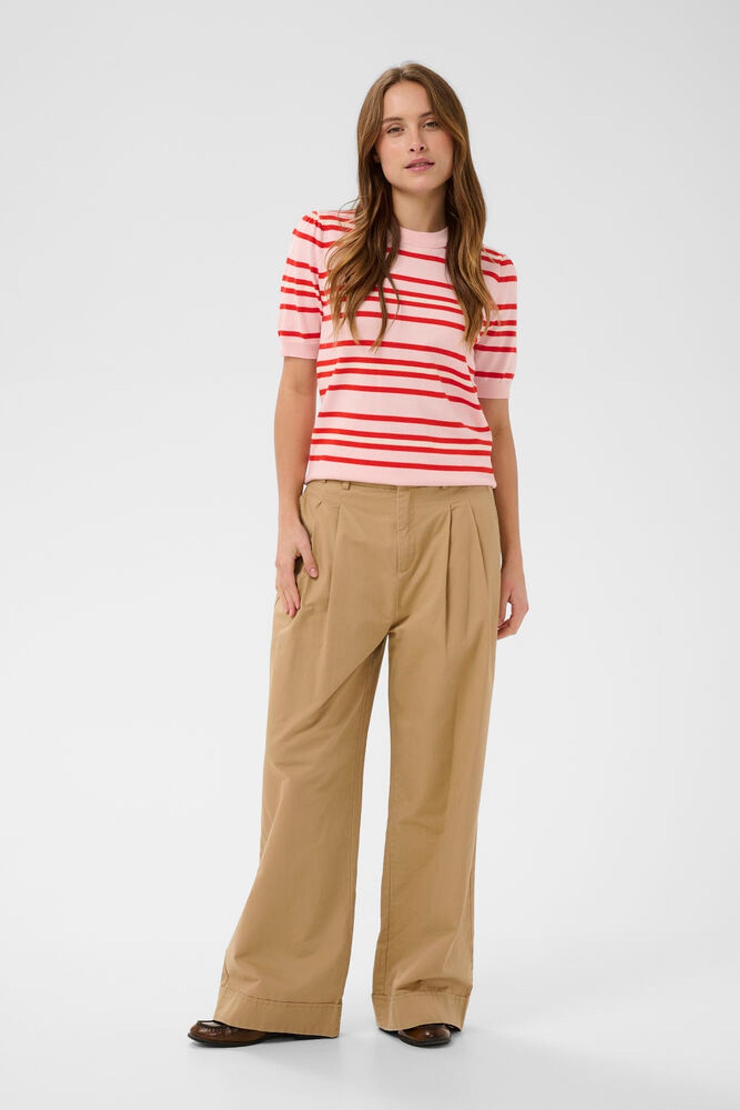 Model in beige trousers with short sleeve pink knit and red stripes