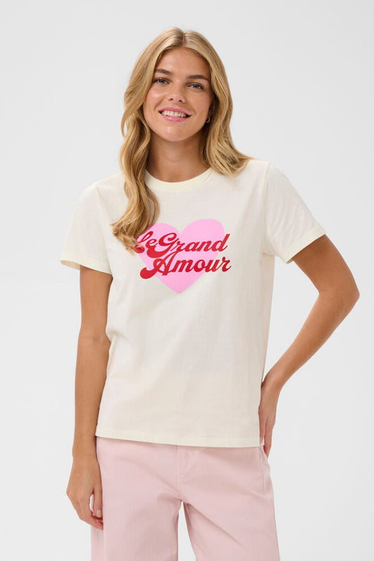 Woman wearing a white t-shirt with 'Le Grand Amour' text and pink heart design on a plain background