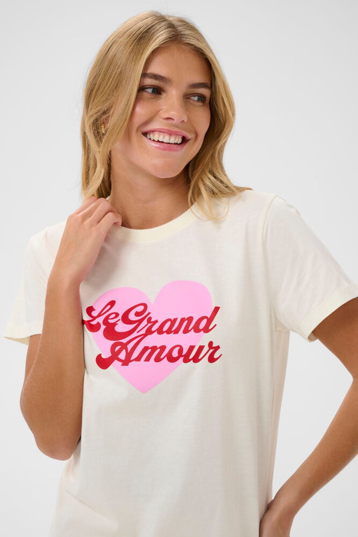 Woman wearing a white t-shirt with a pink heart and red text design on a plain background