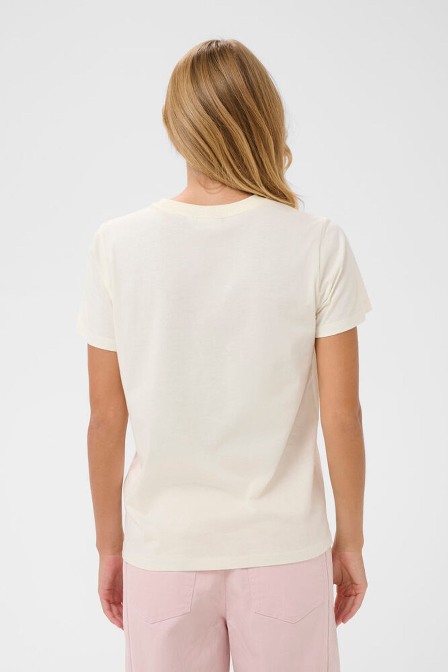 Woman wearing a white t-shirt and pink pants on a light gray background