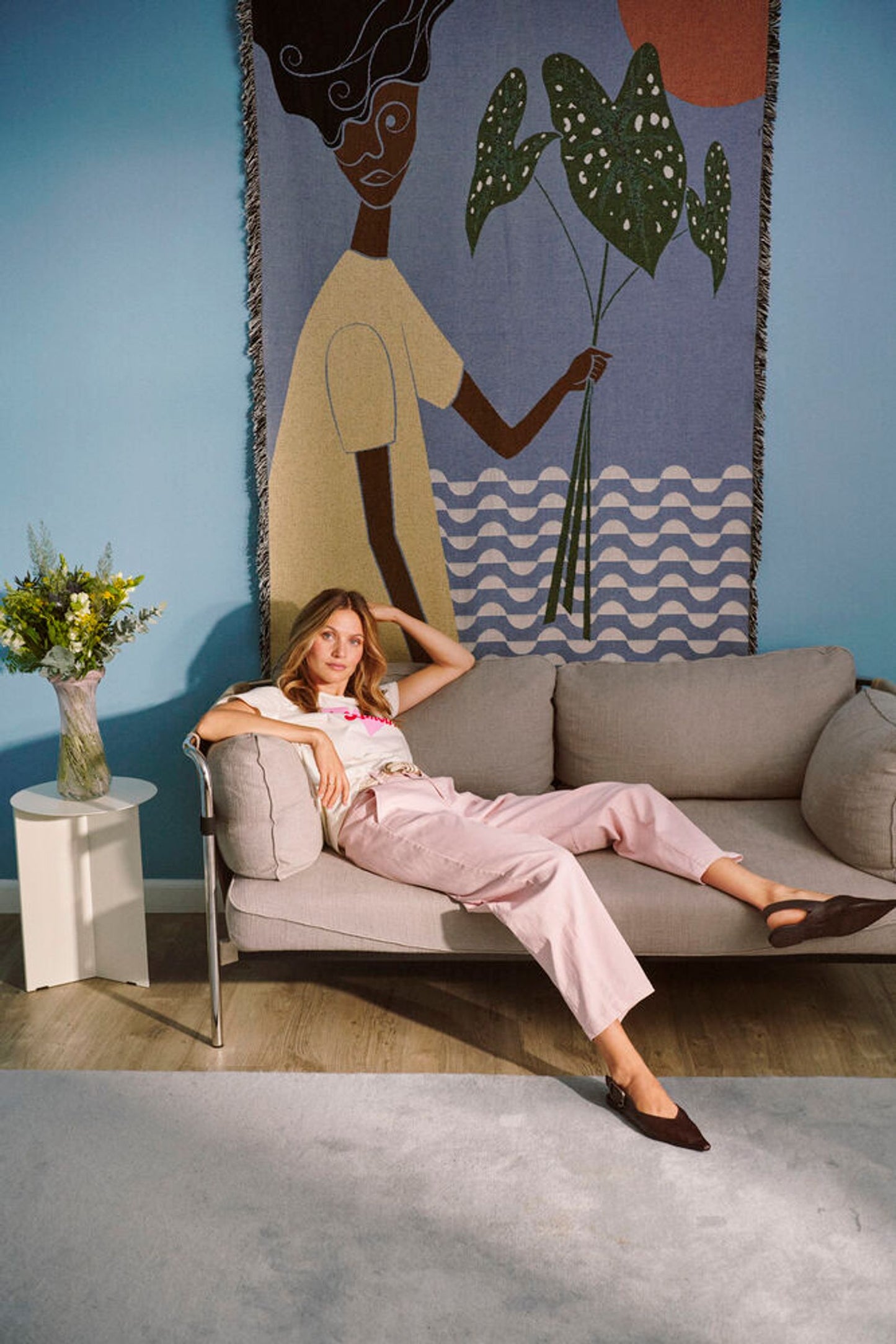 Woman sitting on a couch in a room with a large wall tapestry.