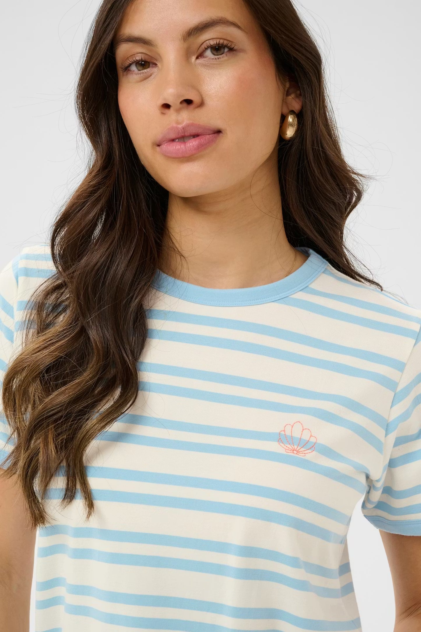Woman wearing a striped t-shirt with a small logo on a plain background