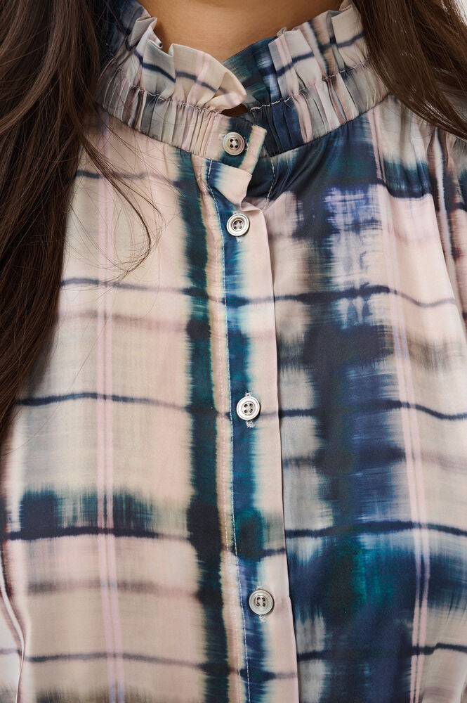 Close-up of a women's button-front blouse with a ruffled high collar, featuring a blue, teal, and cream tie-dye plaid pattern.
